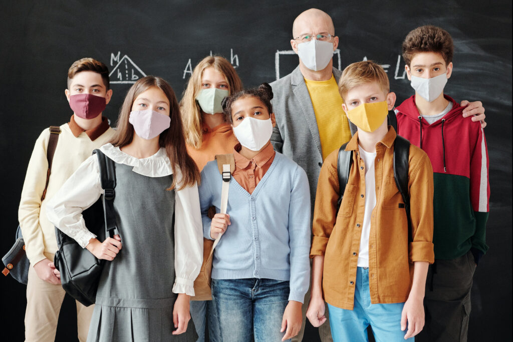 Zdjęcie przedstawiające nauczyciela z uczniami w maseczkach na twarzach.