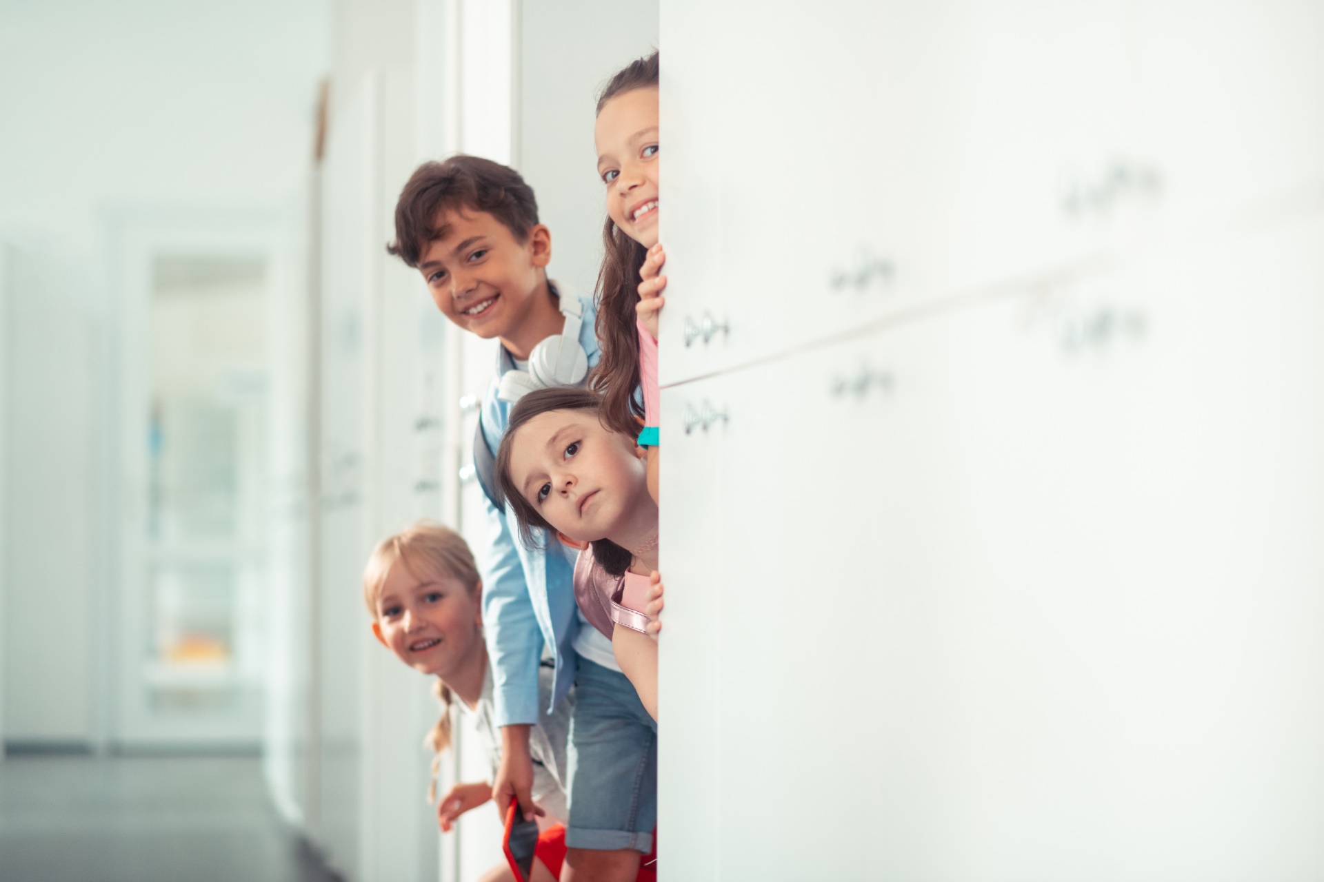 Chłopiec i dziewczęta uśmiechnięci wychylają się zza ściany podczas przerwy w szkole.