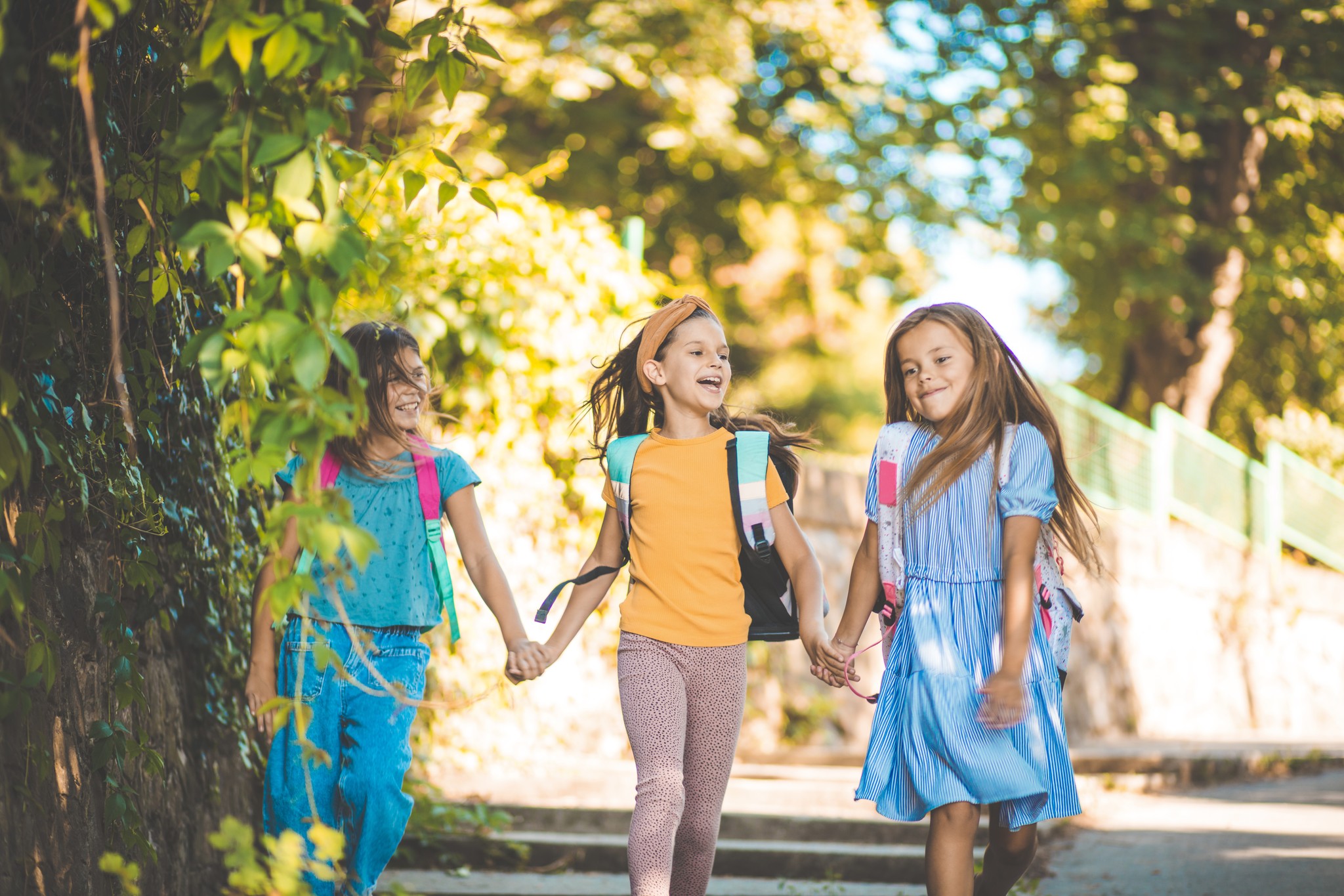 Trzy małe, radosne dziewczynki spacerujące po parku.